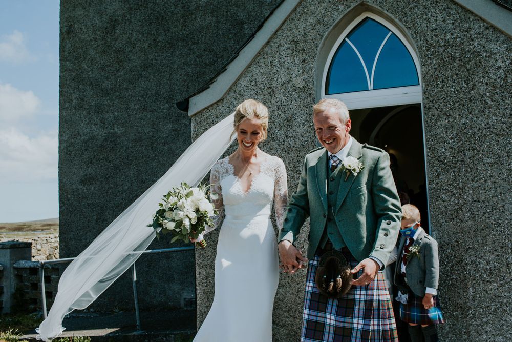 Wedding couple outside a rustic stone church with a blue arched window.