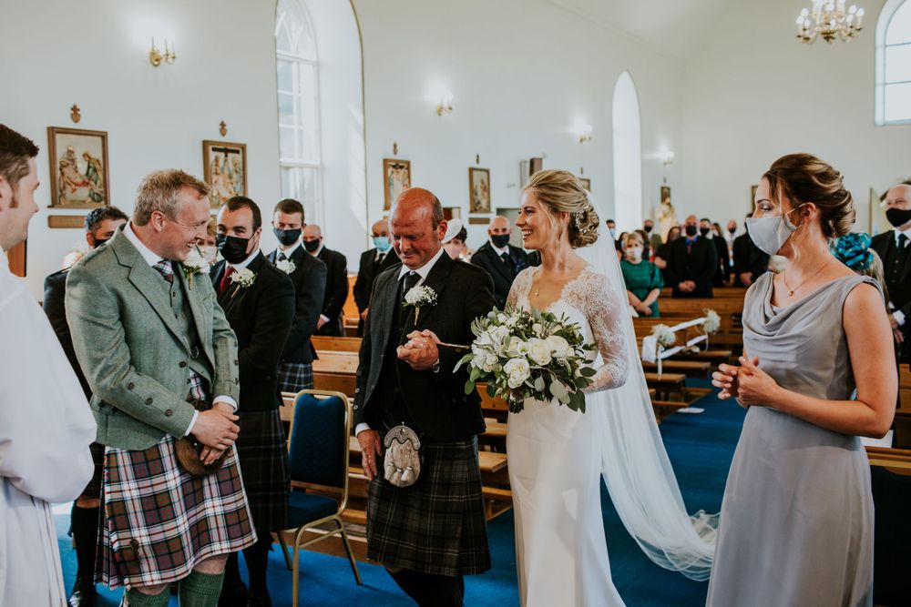 Traditional Scottish wedding ceremony with kilts and formal attire in a bright church setting.