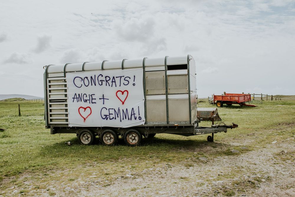 Rustic trailer in a field with congratulatory wedding message written on its side.