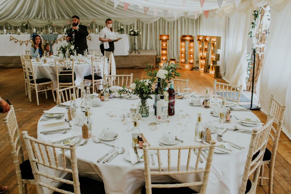 Elegant wedding reception table setting with white linens and floral centerpieces in a draped tent venue.