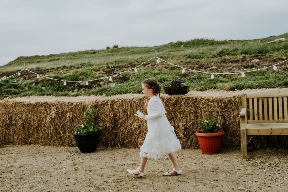 Bride walking past hay bales and wooden bench in outdoor rustic setting.