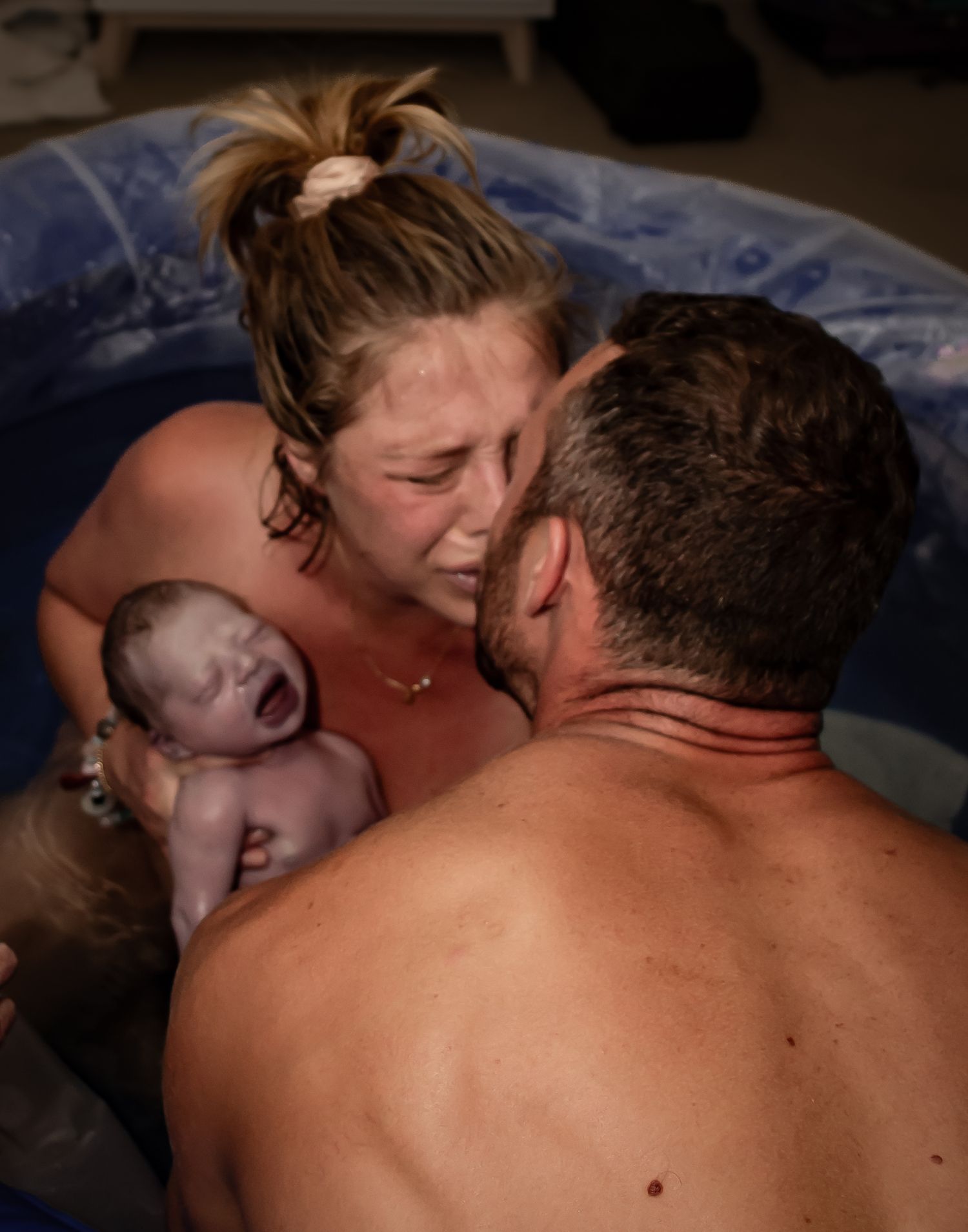 Image of a mother kissing her husband while holding her newborn baby after just giving birth.