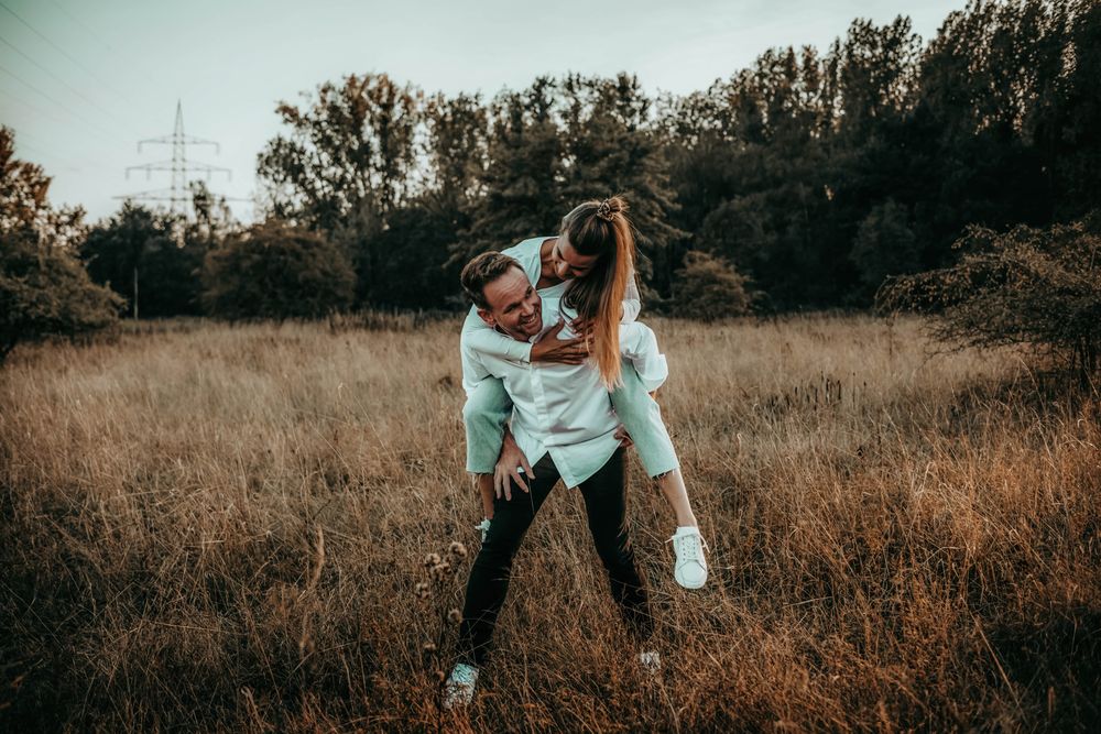 Playful couple embraces in a golden autumn field at sunset with moody lighting and warm tones.