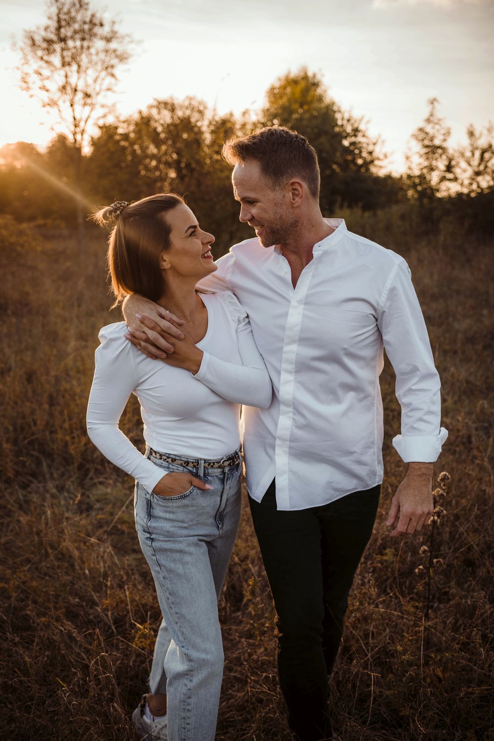 Romantic couple in casual white outfits share an intimate moment in a sunlit autumn field.