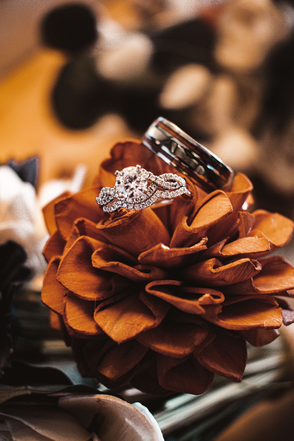 Wedding rings displayed on an autumn-colored rose with diamond engagement ring detail.