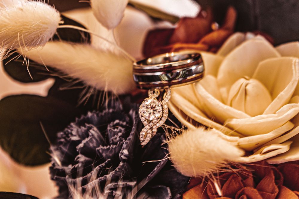 Wedding rings displayed artistically among soft cream and burgundy artificial flowers.