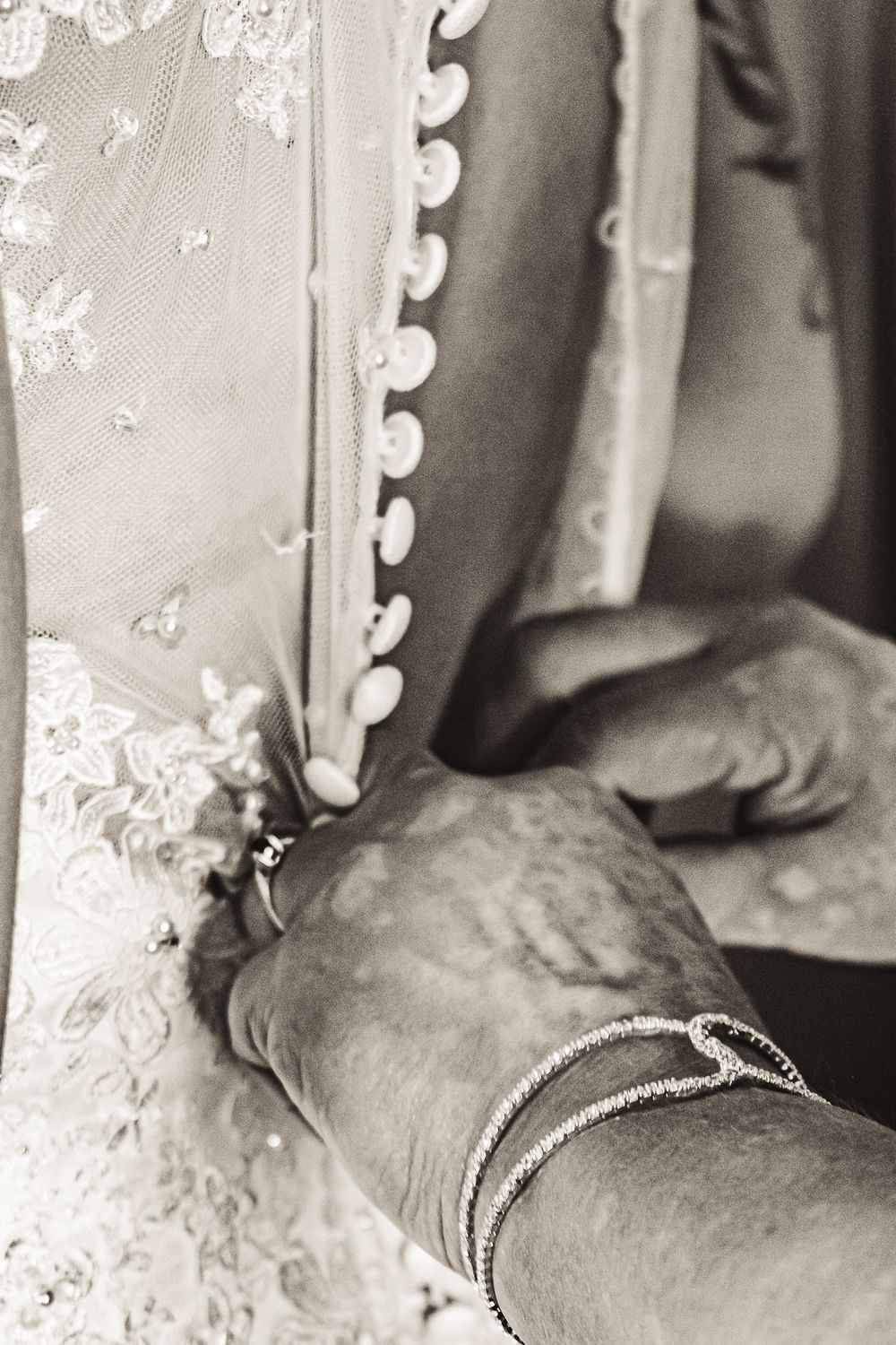 Detail shot of vintage lace buttons being fastened on a wedding dress.