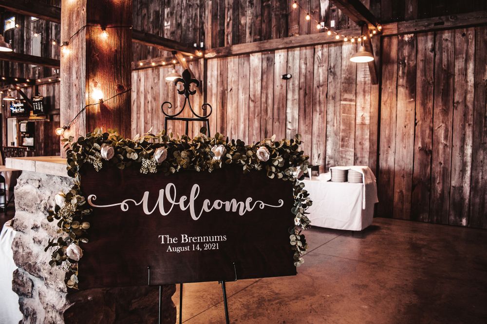 Rustic wooden welcome sign decorated with greenery at a barn wedding venue.