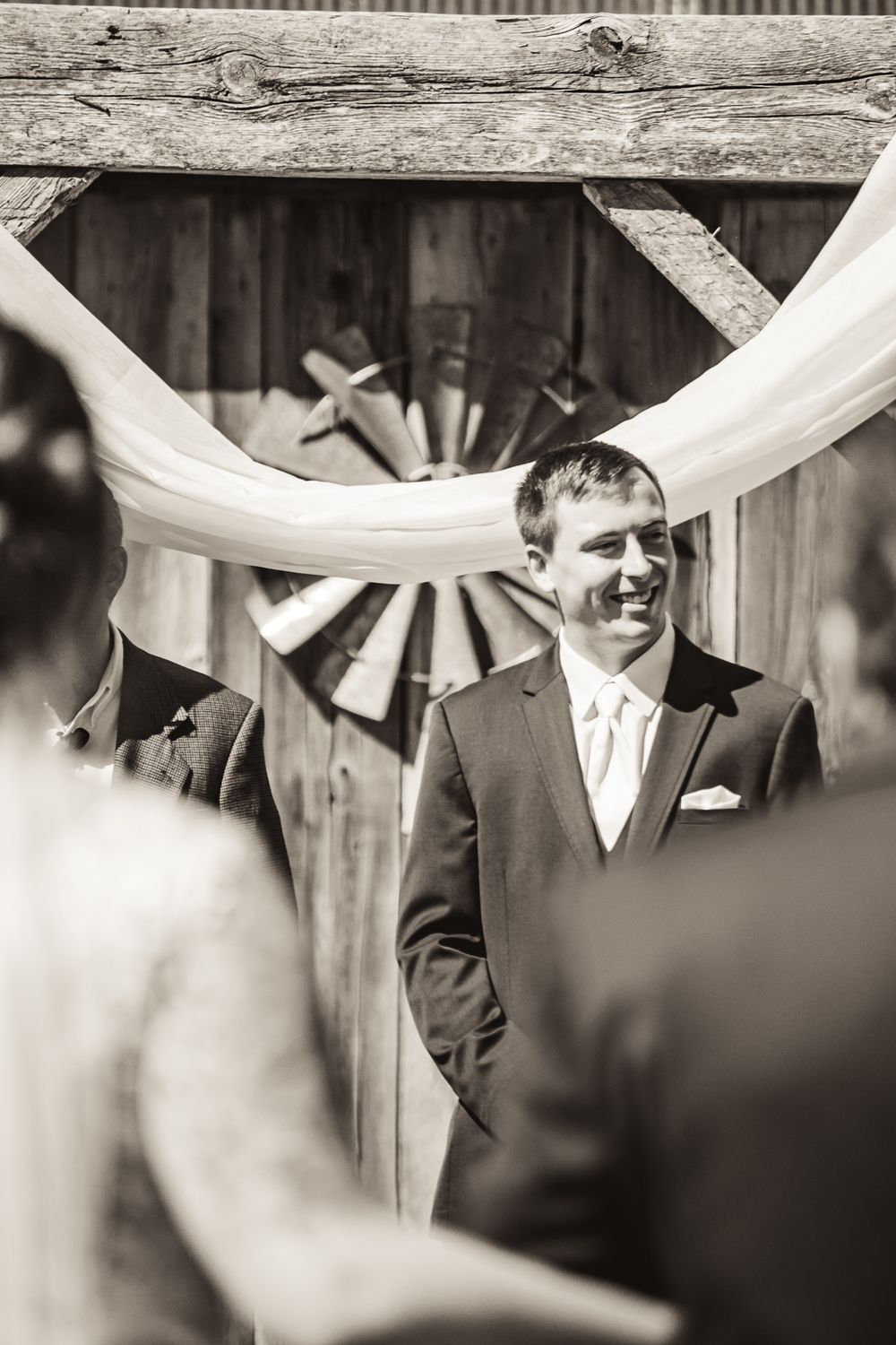 Black and white wedding ceremony photo with white fabric draped decoratively against wooden backdrop.