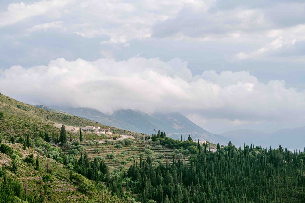 Mountain landscape with terraced hillsides and cypress trees under cloudy skies.
