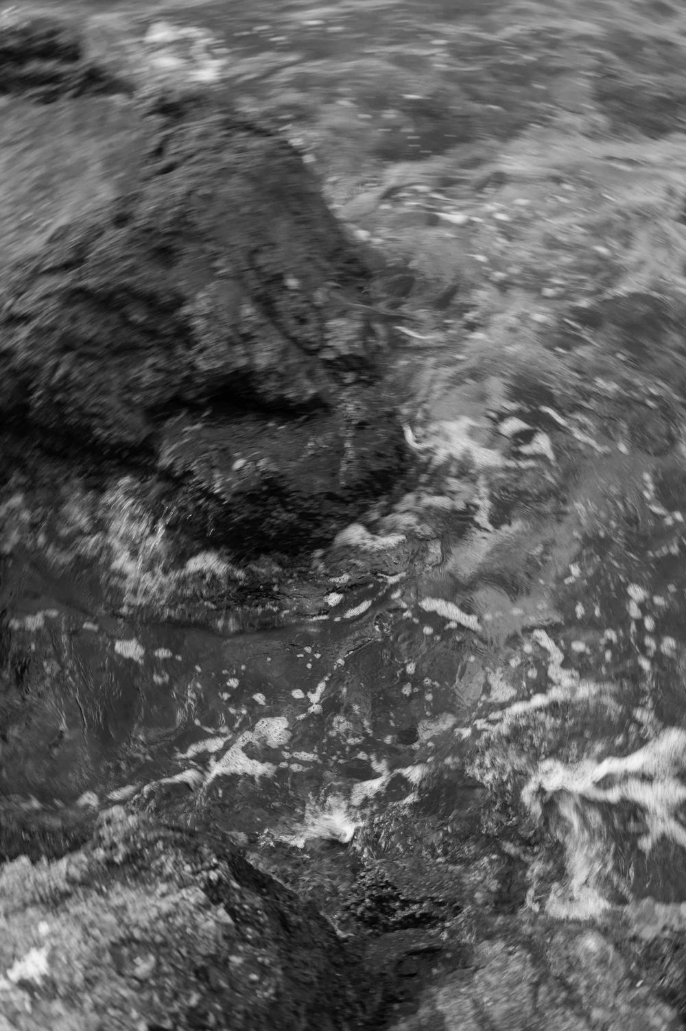 Black and white close-up of rushing water and rocks creating dynamic patterns.