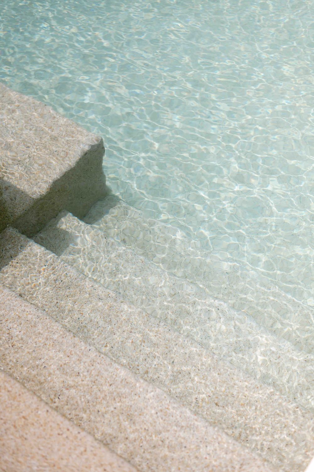 Crystal clear turquoise water meeting stone pool edge in Mediterranean setting.