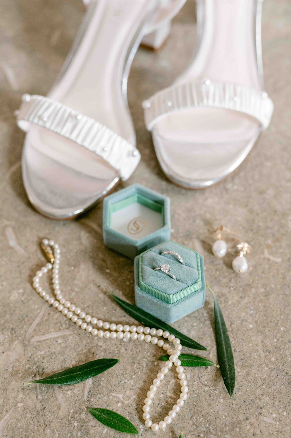 Wedding accessories including white heels, pearl necklace, and mint green ring boxes with olive leaves.