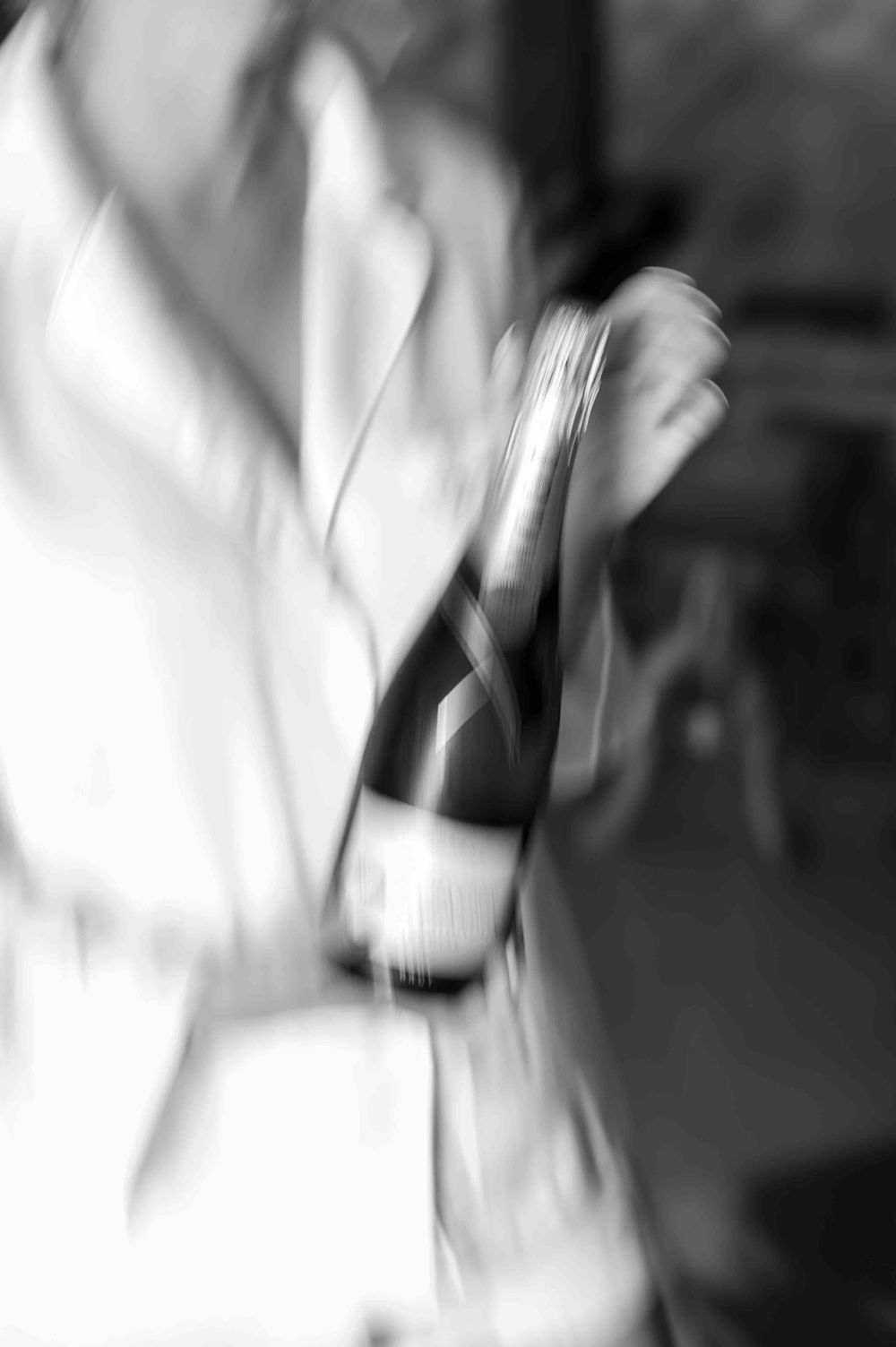 Motion-blurred black and white photo of a champagne bottle being handled.