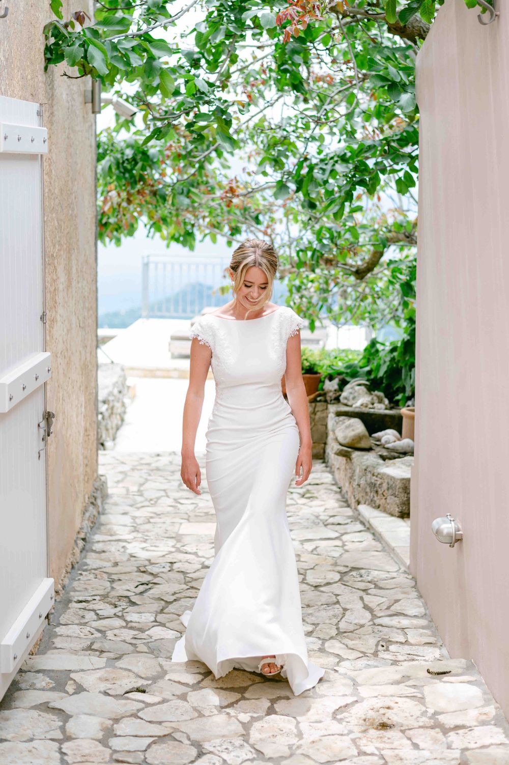 Bride walking down a stone path in a classic white wedding dress with Mediterranean views.