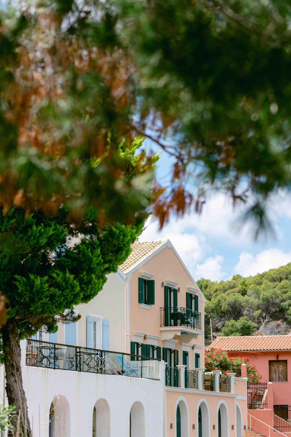 Mediterranean-style villa with green shutters and balcony surrounded by trees.