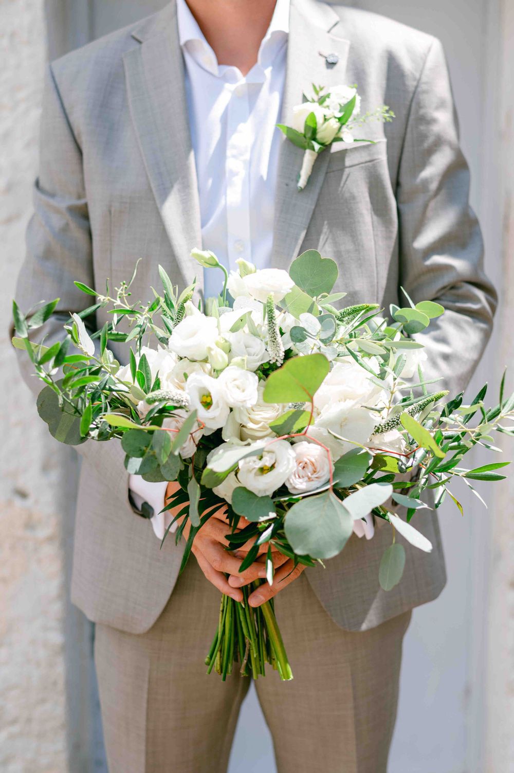 Elegant white and green wedding bouquet held against a light grey suit.