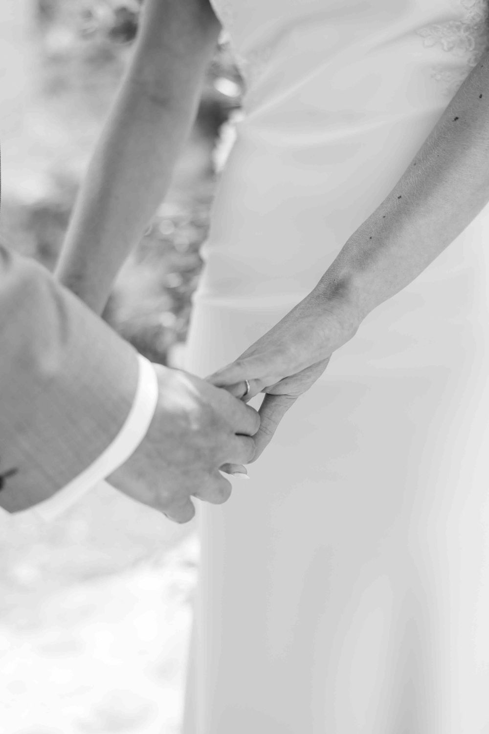 Close-up black and white photo of couple holding hands during wedding ceremony.