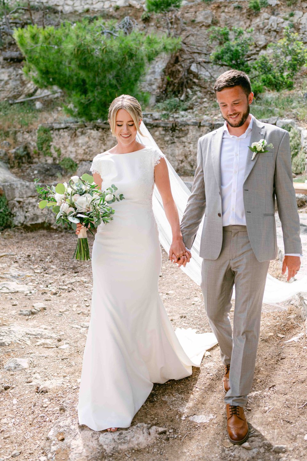 Couple walking hand in hand after wedding ceremony, bride carrying white bouquet.
