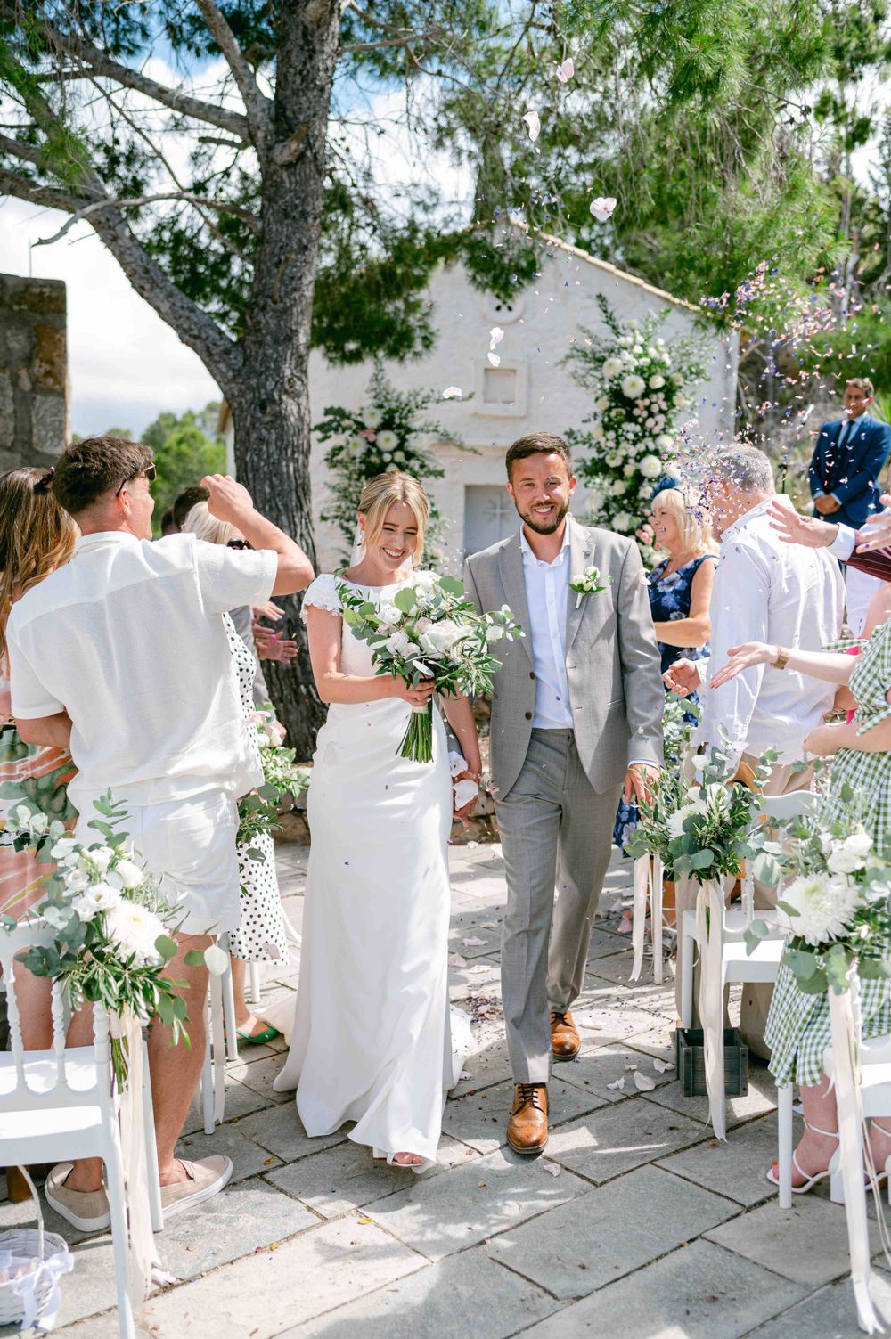 Wedding recessional with couple walking down aisle decorated with white flowers and greenery.