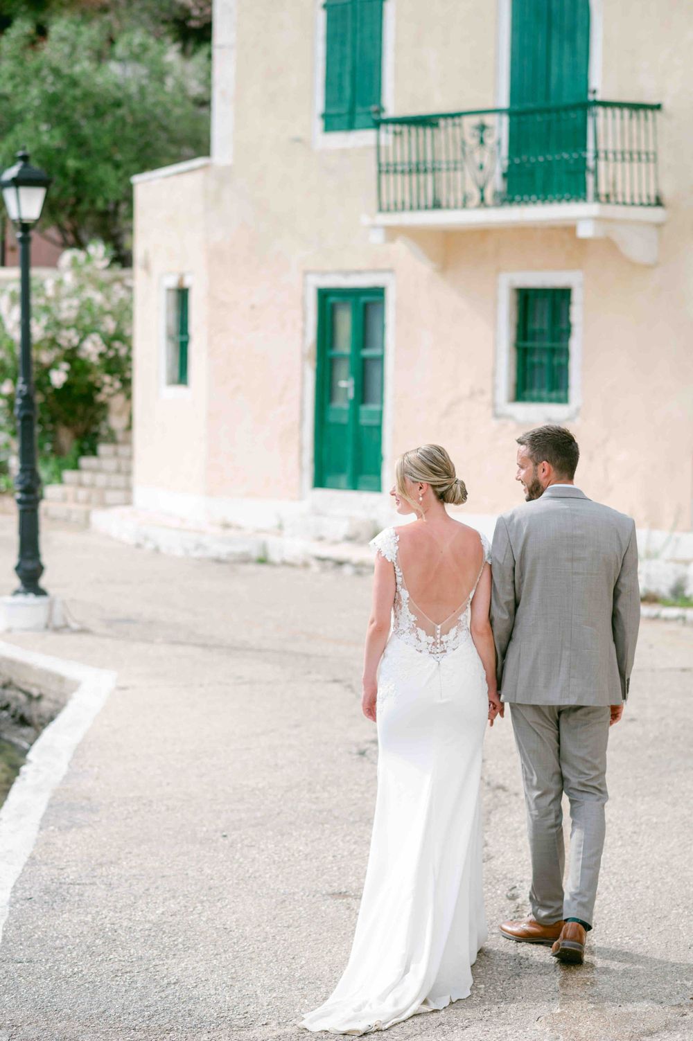 Romantic walking shot of couple outside Mediterranean building with green shutters.