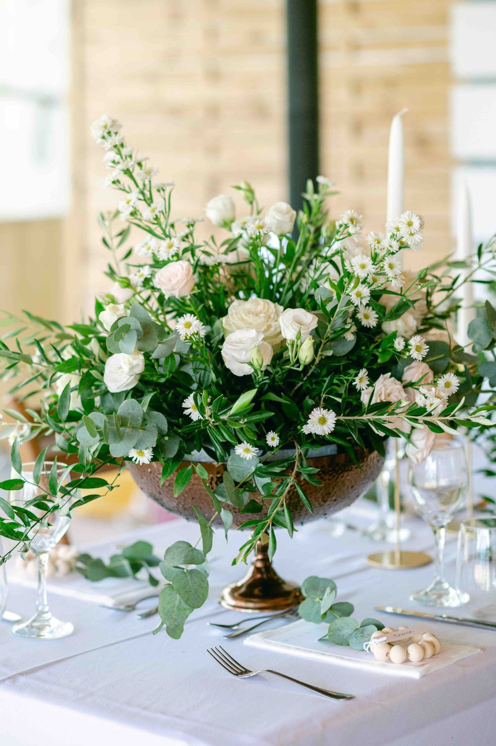 Elegant table centerpiece with white flowers and eucalyptus in gold pedestal vase.
