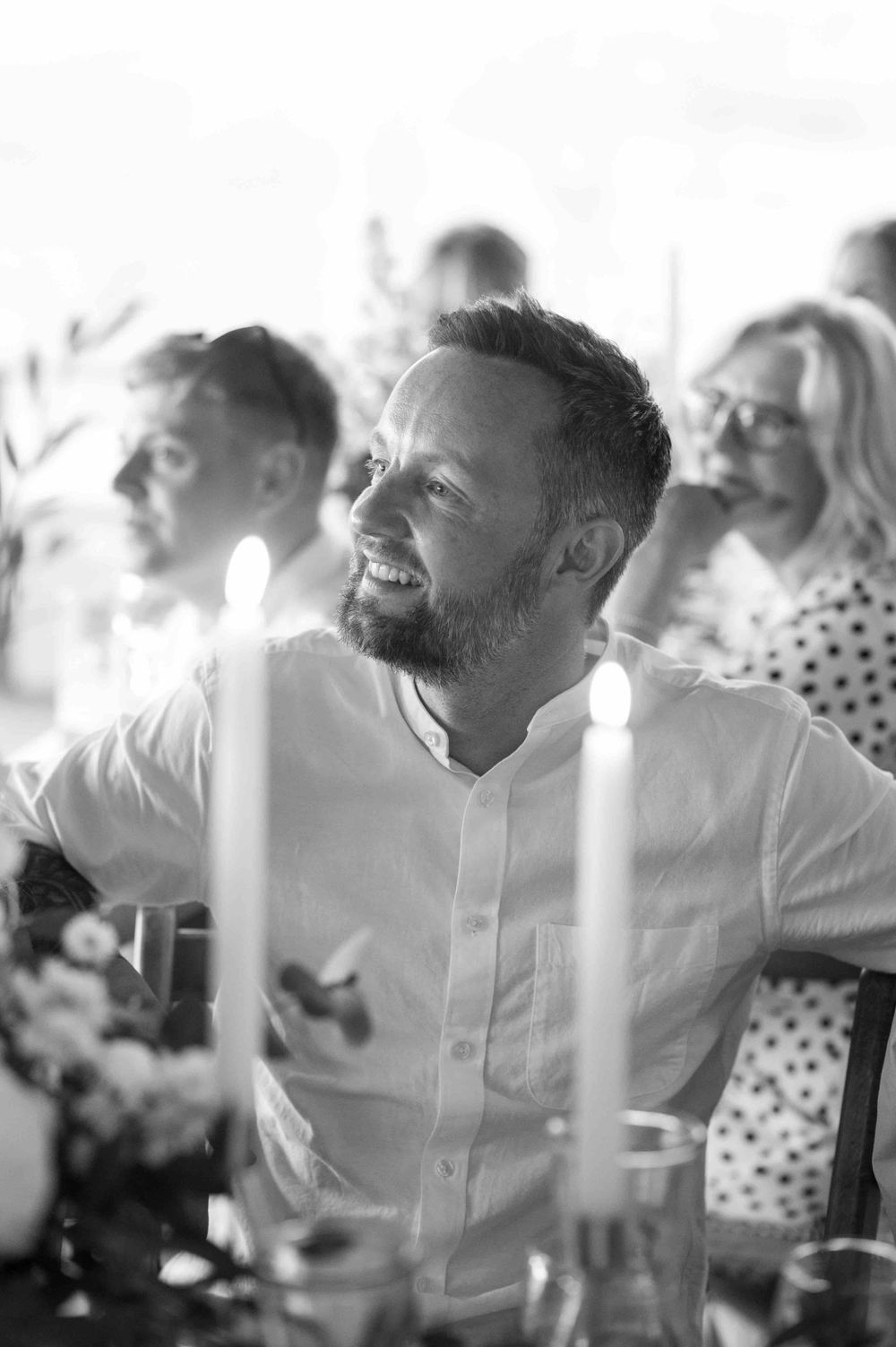 A black and white candid photo of wedding guests enjoying themselves at an outdoor reception.