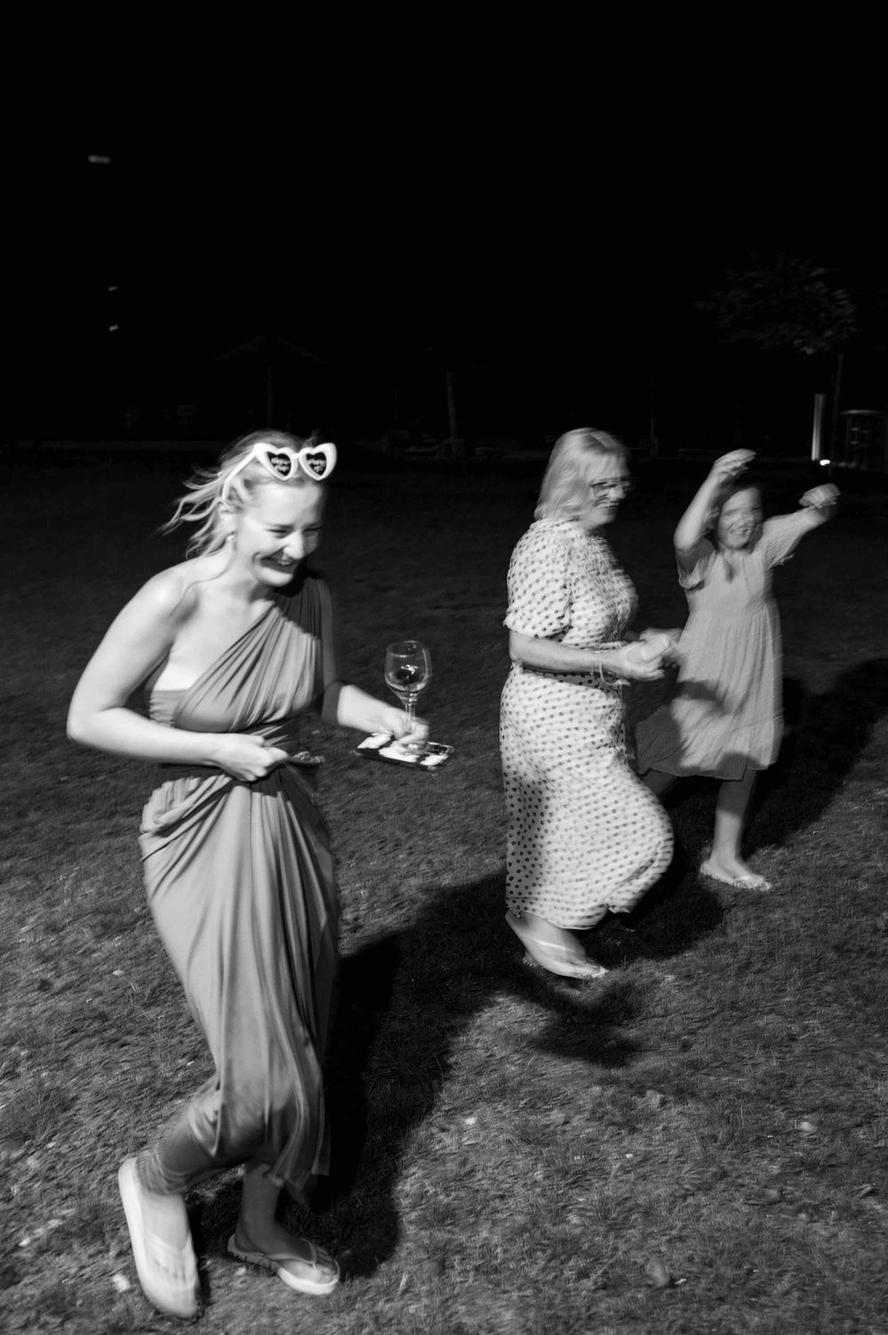 A black and white photo of guests dancing outdoors at a nighttime celebration.