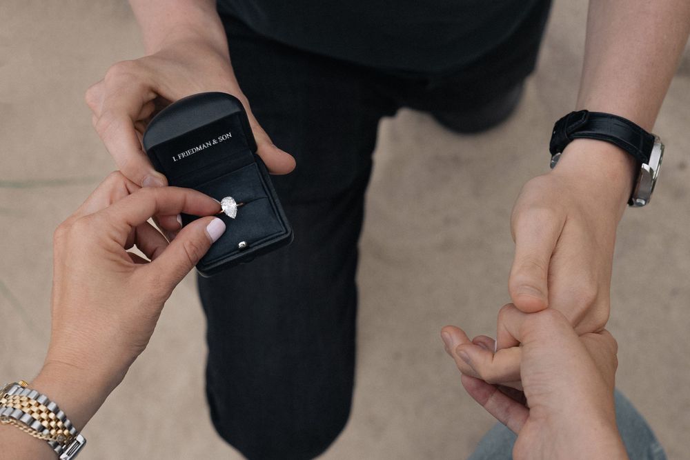 Close-up of hands exchanging a ring in an outdoor proposal moment.
