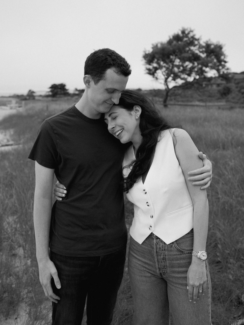 An intimate black and white portrait of a newly engaged couple on a grassy hillside.