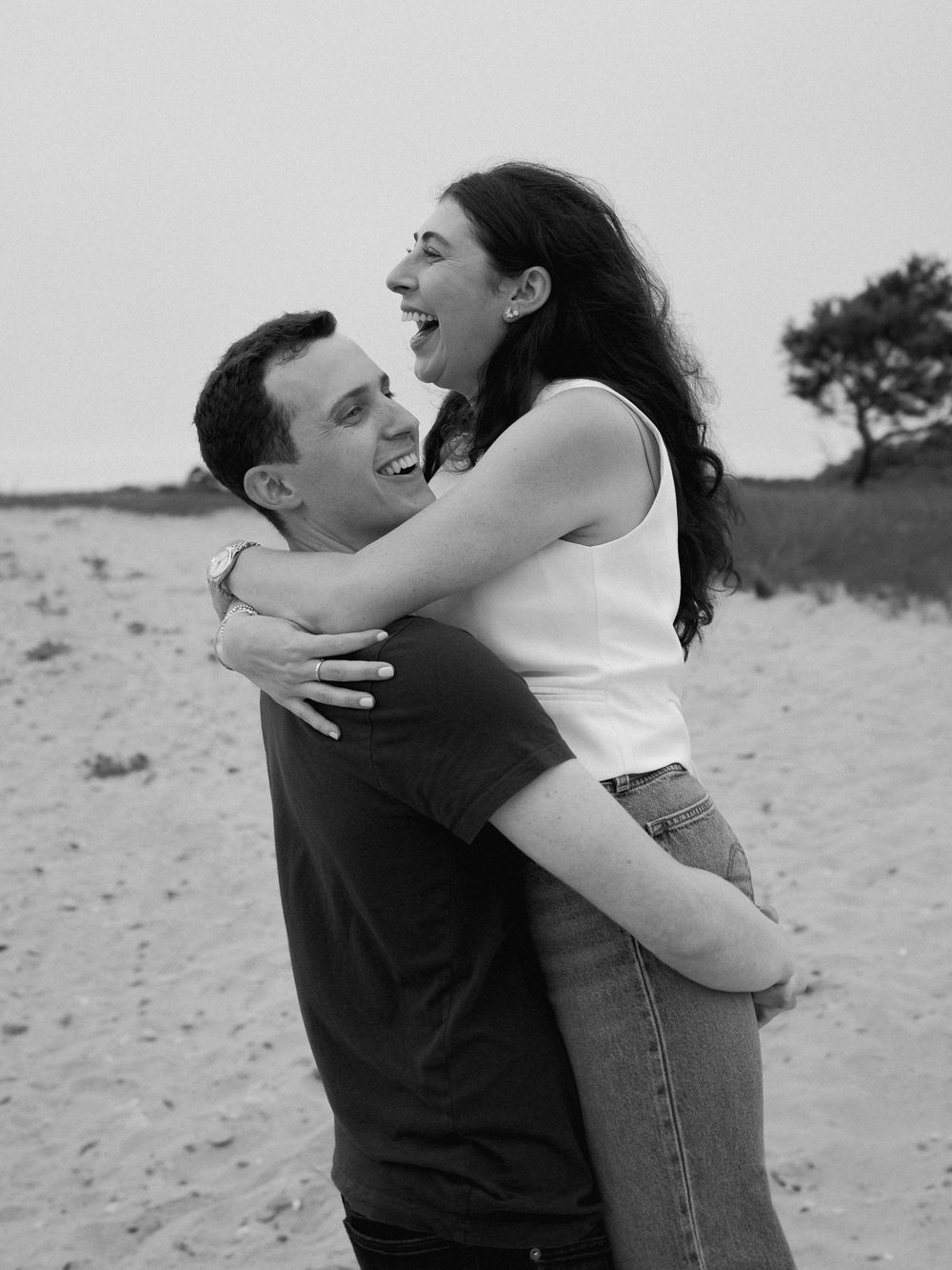 A joyful embrace captured in black and white on a beach after a proposal.