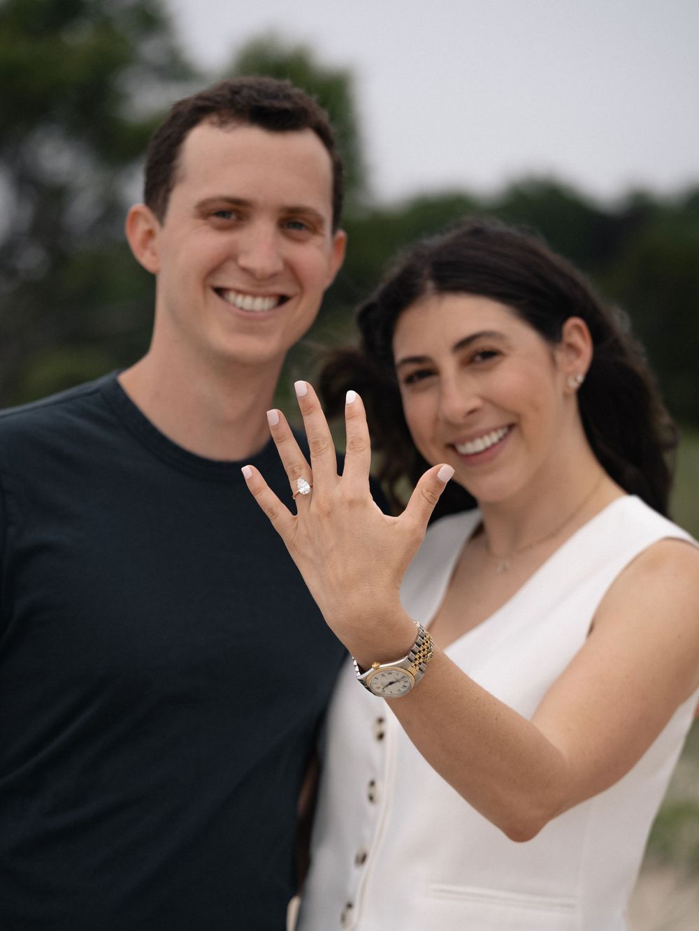 A happy couple showing off their new engagement ring on the beach.