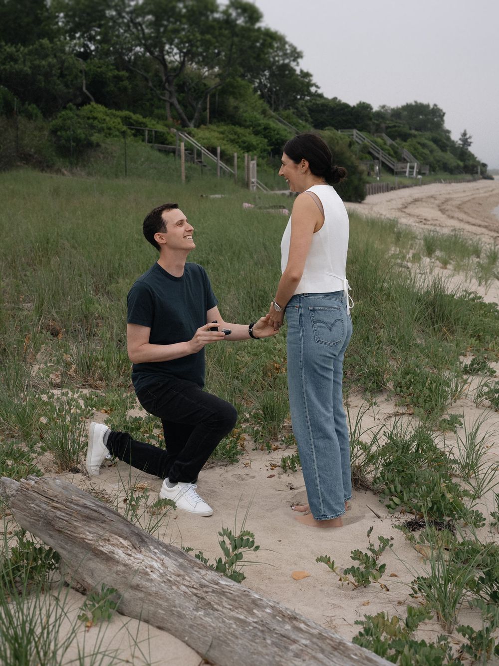 A surprise beach proposal moment with two people on sandy dunes.