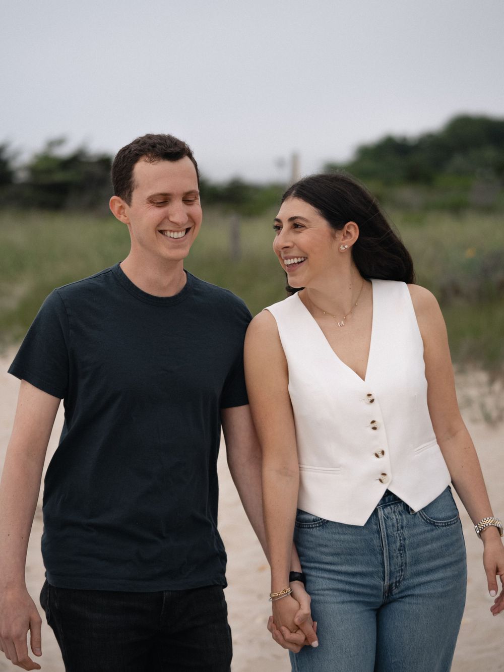 A happy couple walking hand in hand along a sandy beach path.