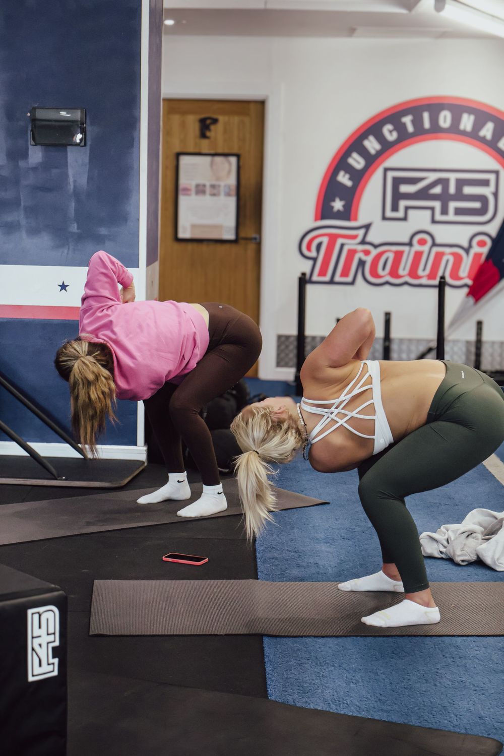 Two women bending forward during a stretching workout session at an F45 Training gym.