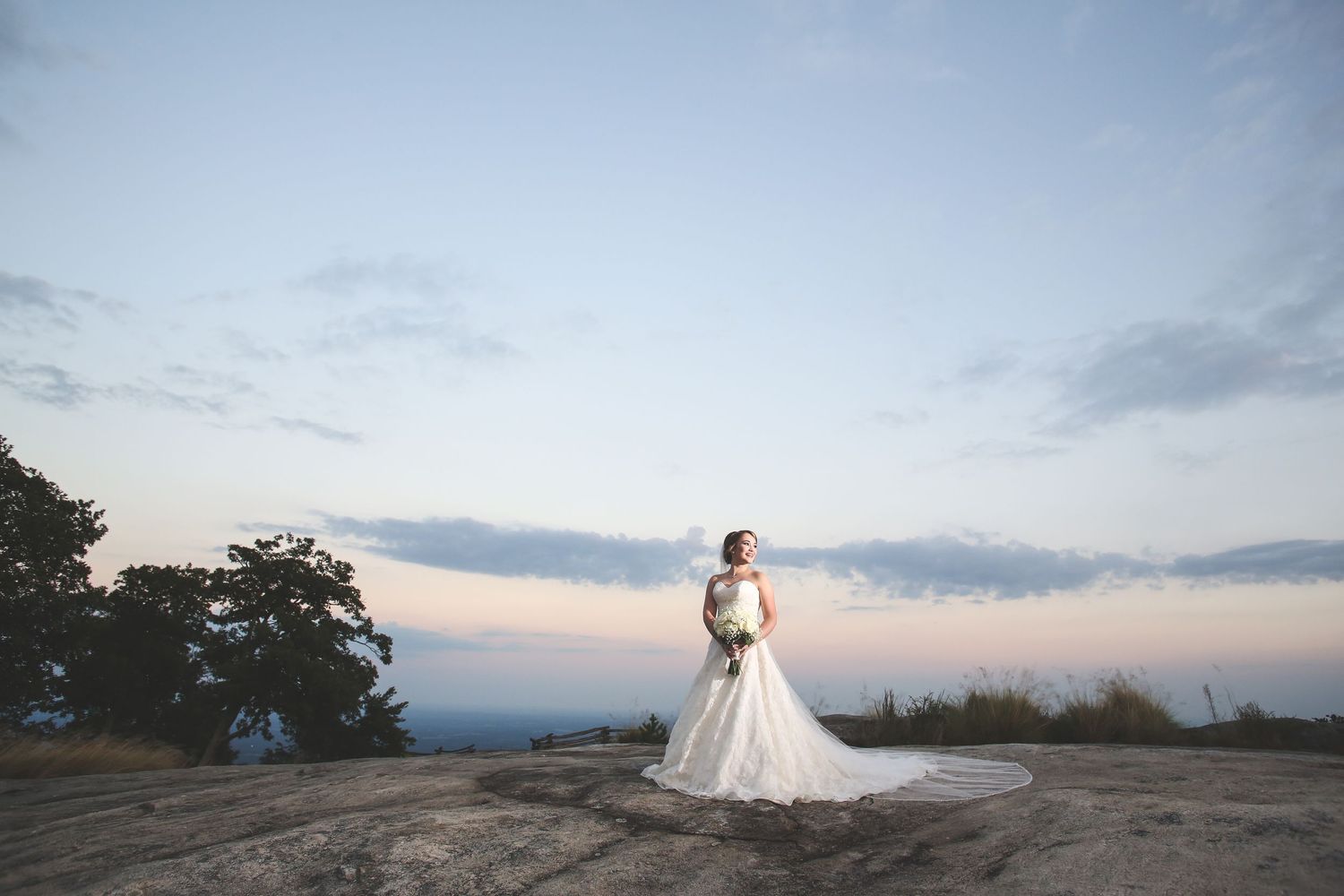 Silhouette of person in wedding dress against sunset sky on mountain overlook.
