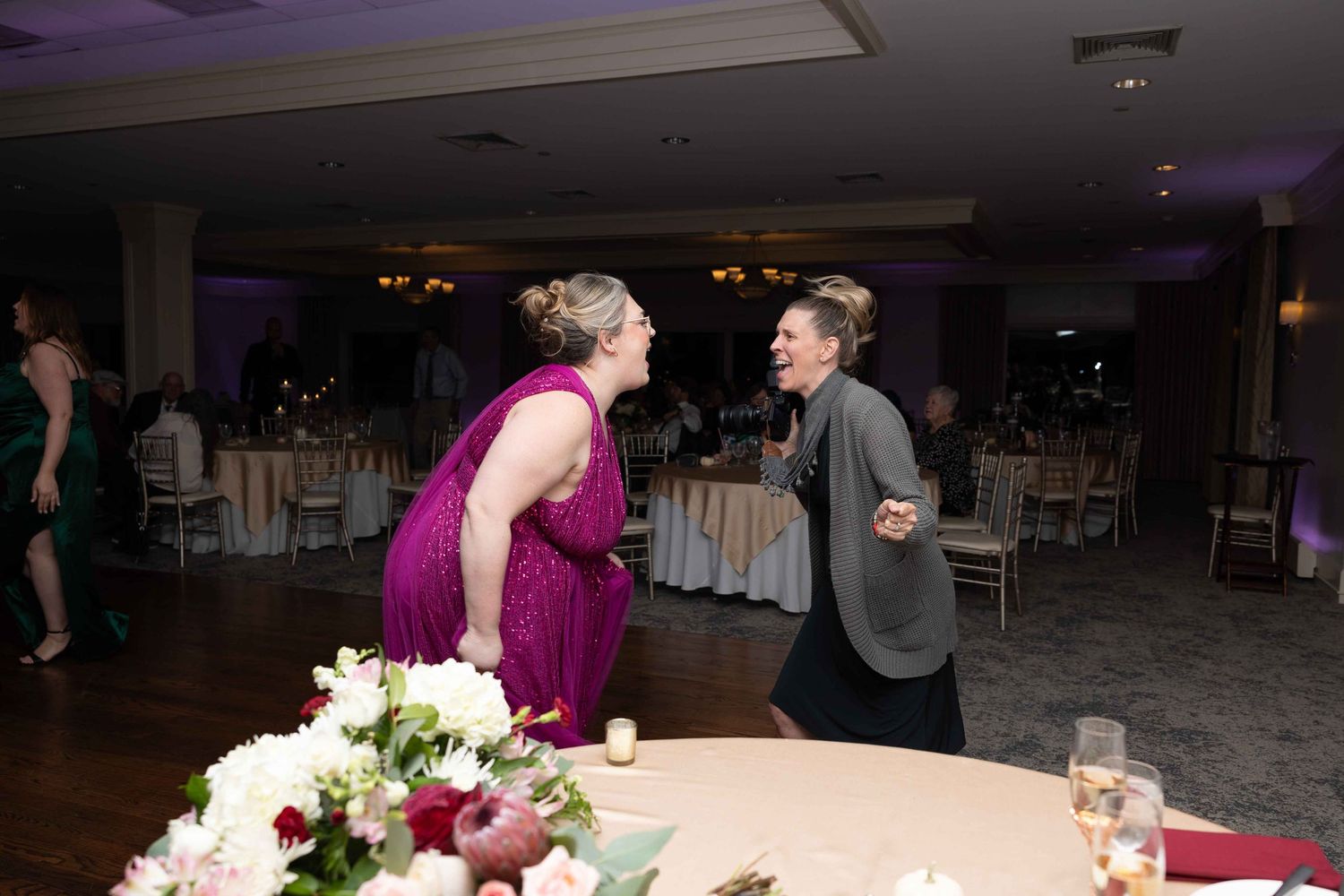 Two people having an animated conversation on a dance floor with floral arrangements visible in the foreground.