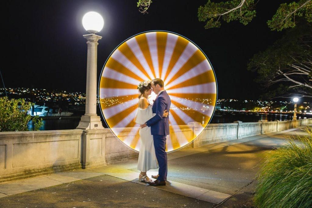 Wedding couple poses against illuminated circular light display at night. Light painting