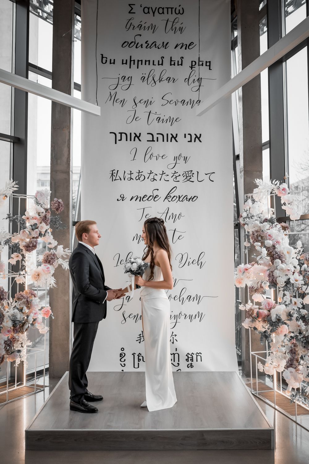 Wedding ceremony space with multilingual 'I love you' wall art and floral decorations.