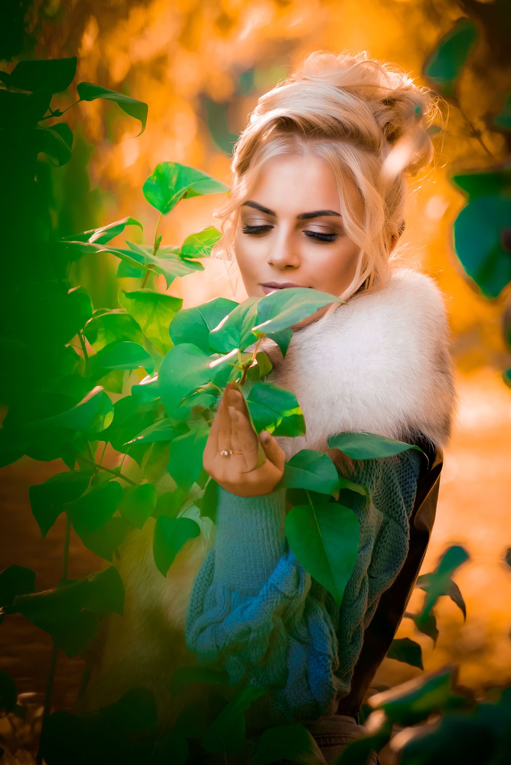 Artistic portrait with soft orange lighting and green foliage creating a dreamy atmosphere.