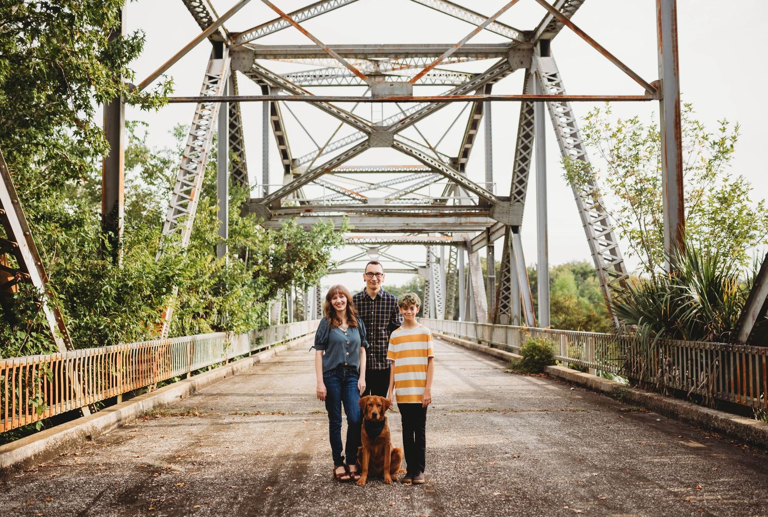 Family poses together on rustic metal bridge during outdoor photo session.