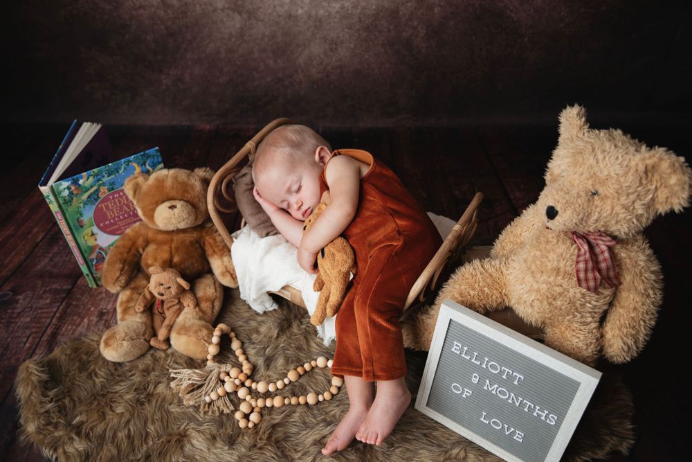 Sleeping baby in rust romper surrounded by teddy bears and a milestone sign reading 4 months of love.