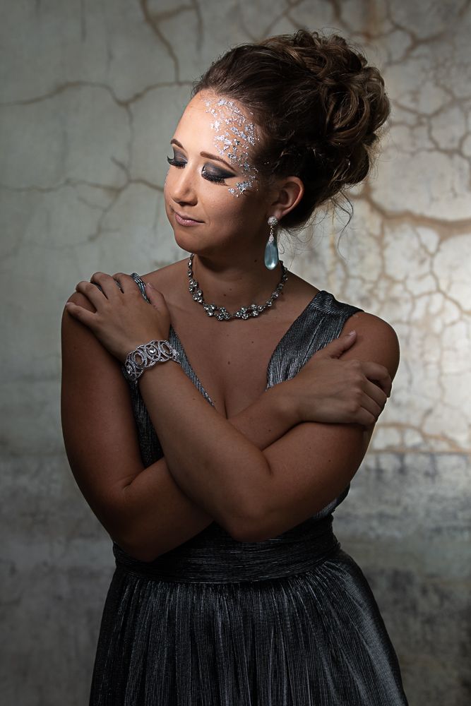 Fashion portrait with silver glitter makeup and jewelry against textured wall background.