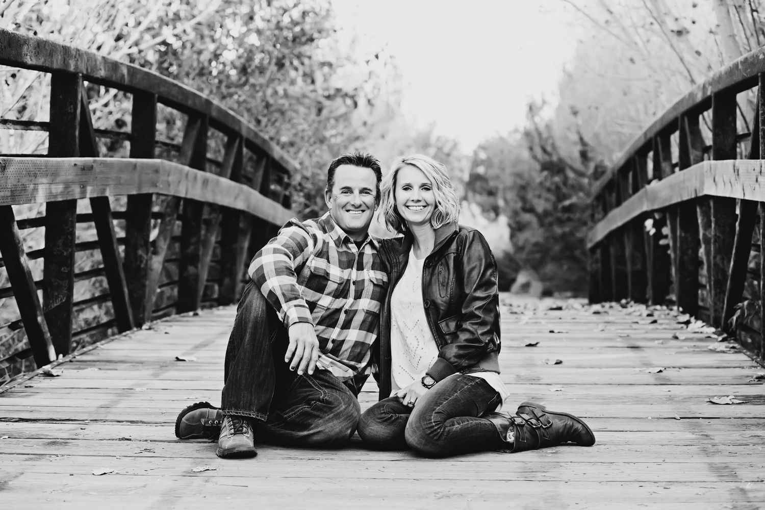 Black and white photo of couple sitting close together on wooden bridge.