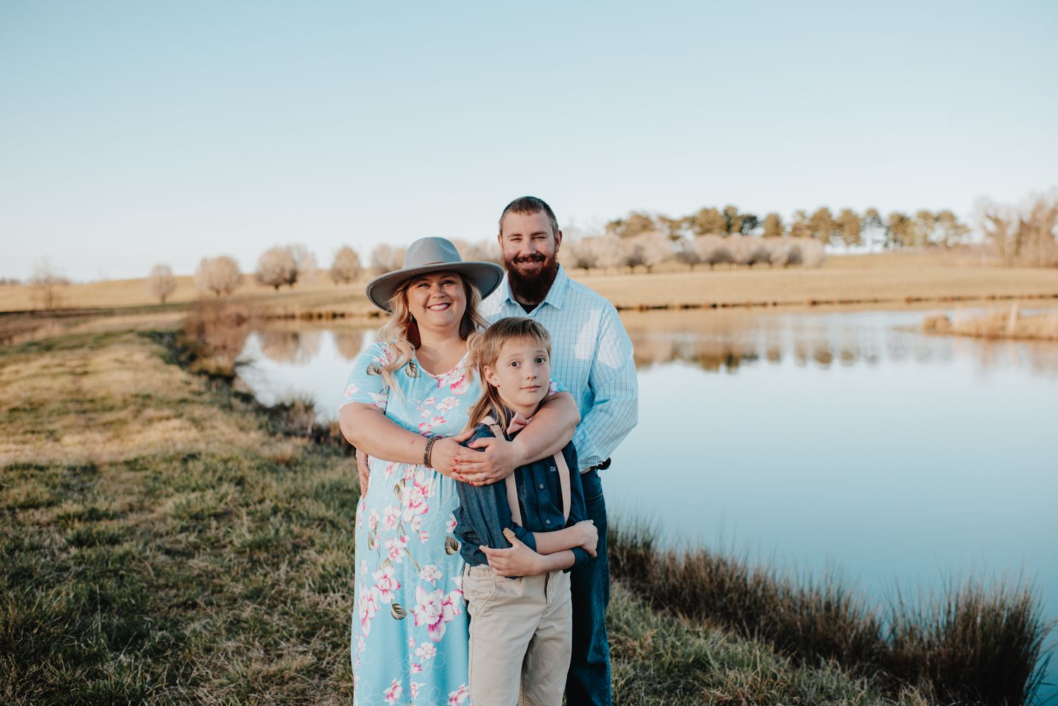 A family poses together for a portrait by a serene lake during sunset.