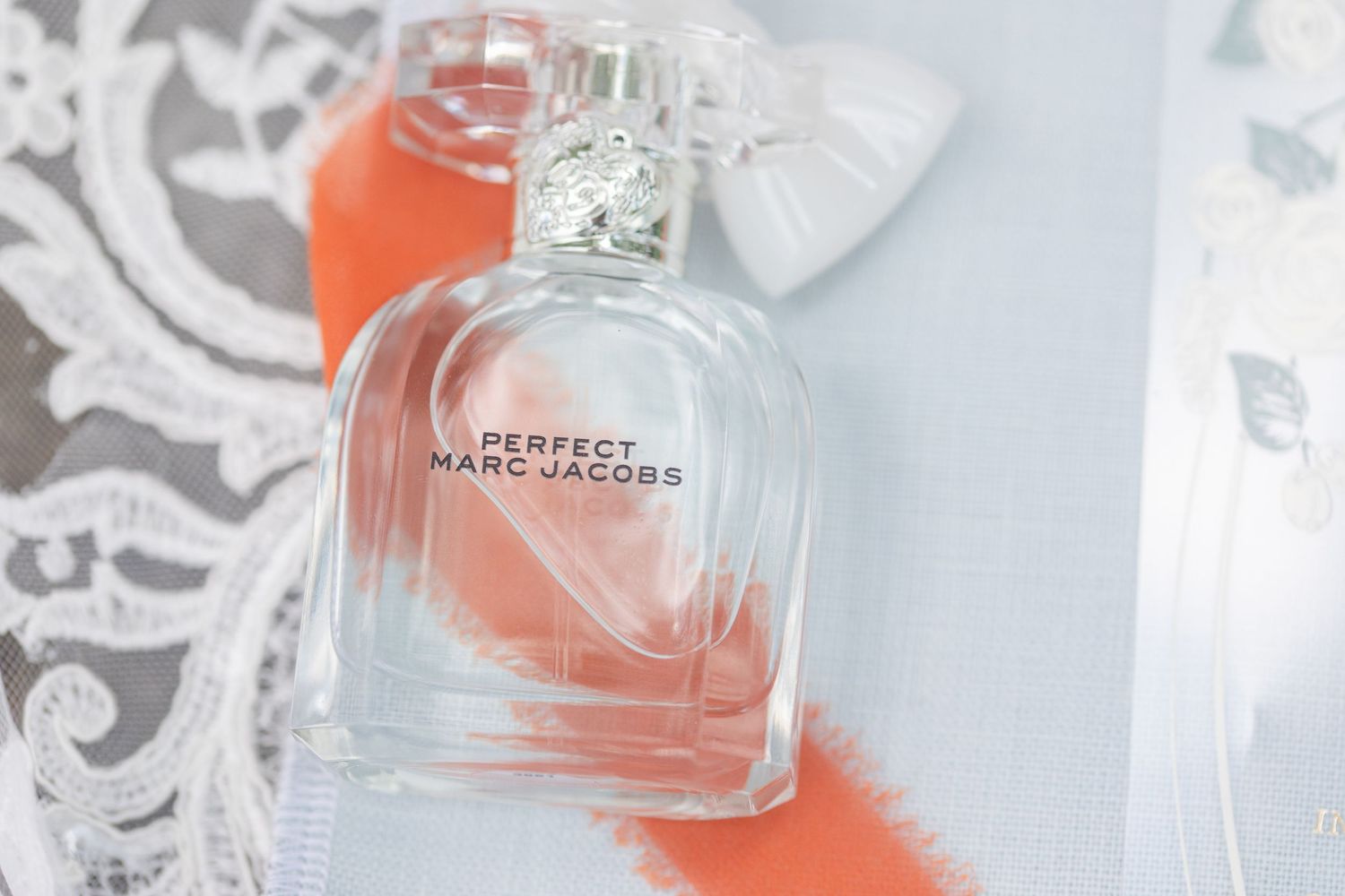 Marc Jacobs perfume bottle photographed on white lace with orange accent.