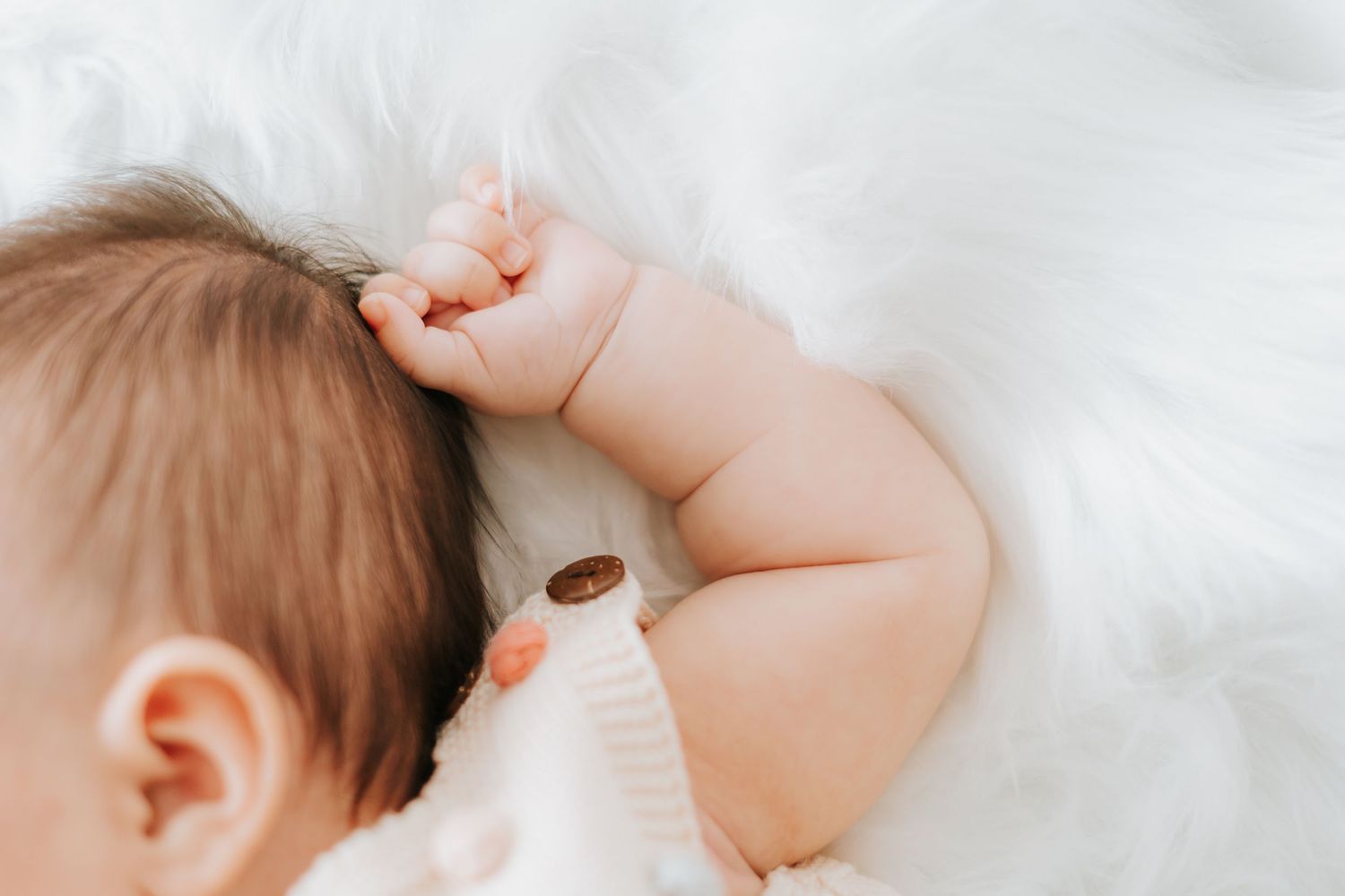 Close-up of a sleeping baby's hand and head against white bedding.