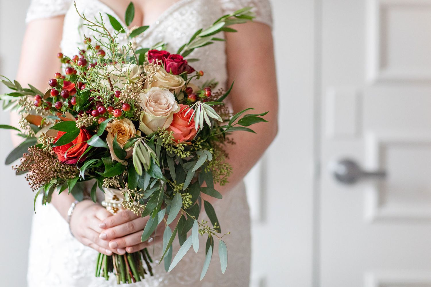 An elegant bridal bouquet featuring red and peach roses with mixed greenery and berries.