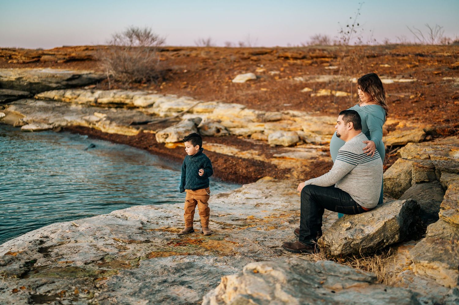 Boy throwing rocks in lake Grapevine while parents watch during maternity photoshoot.