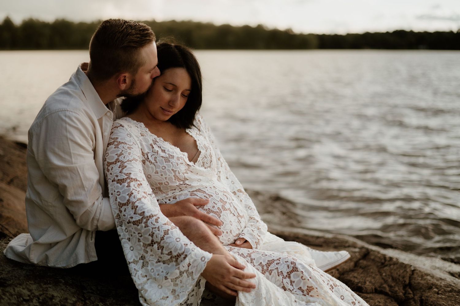 Gravid kvinna och partner sitter på klipporna i solnedgången. Golden hour.